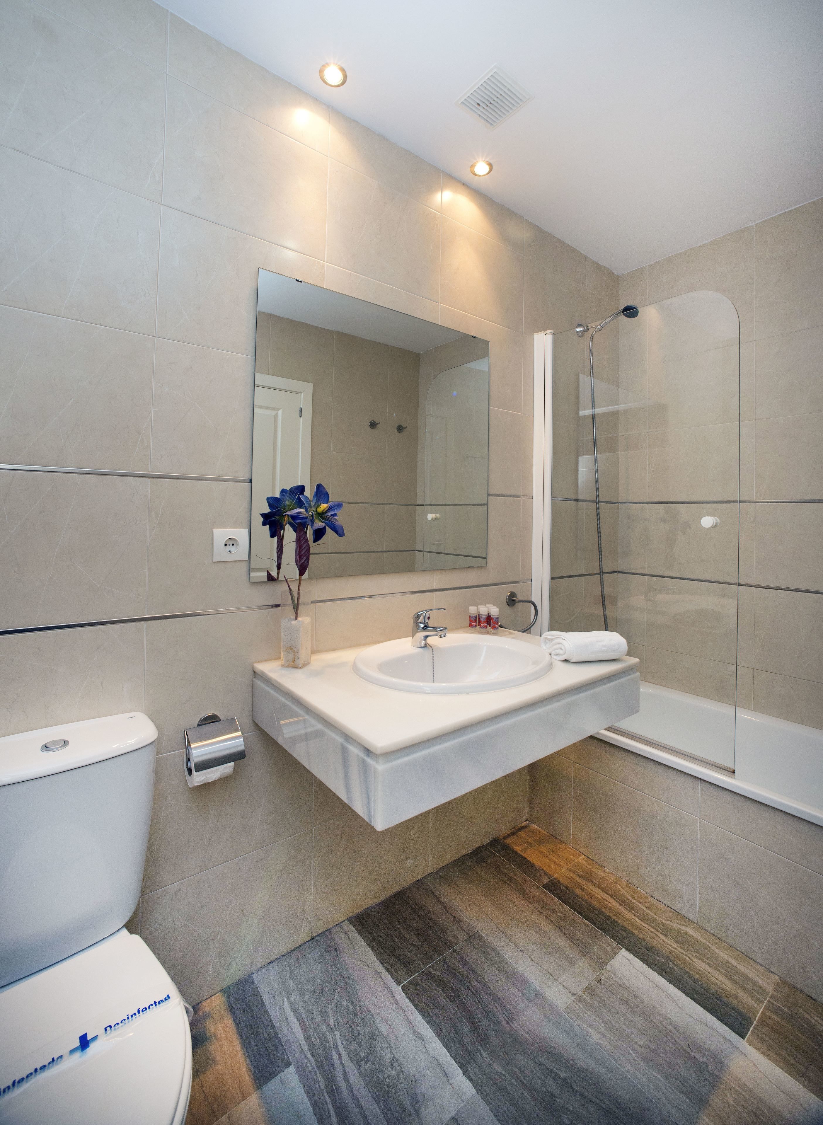 A modern bathroom with a large mirror, a sink, a toilet, and a glass-enclosed shower.