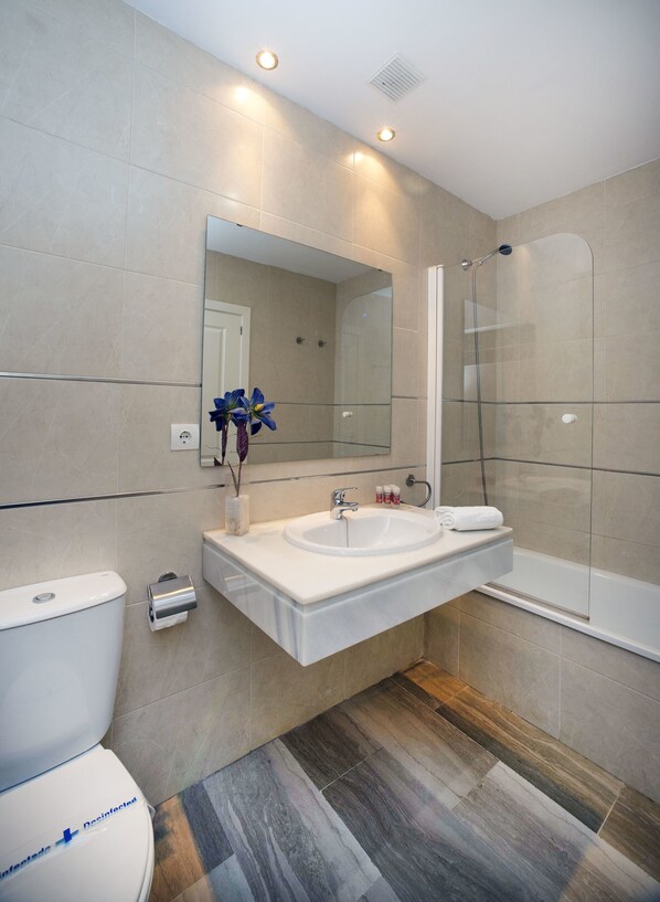 A modern bathroom with a large mirror, a sink, a toilet, and a glass-enclosed shower. - Apartamentos Leo Canela (Ayamonte)