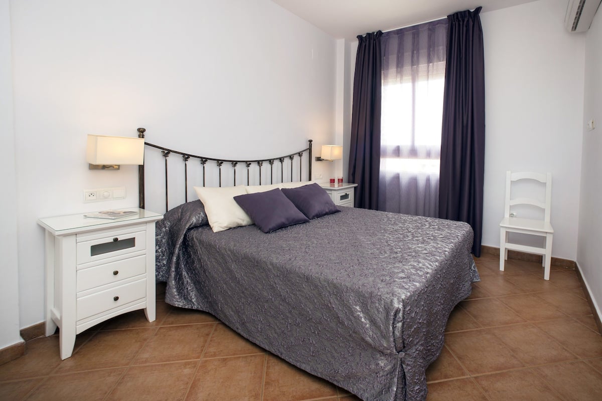 Une chambre bien rangée, avec un lit, des tables de chevet, une chaise et une fenêtre avec des rideaux.