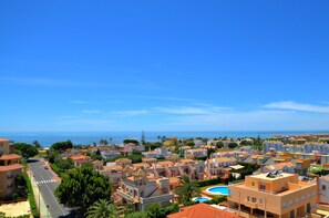 A coastal residential area with a clear view of the sea, featuring a mix of traditional and modern architecture, a swimming pool, and a well-maintained street. - Apartamentos Leo Canela (Ayamonte)