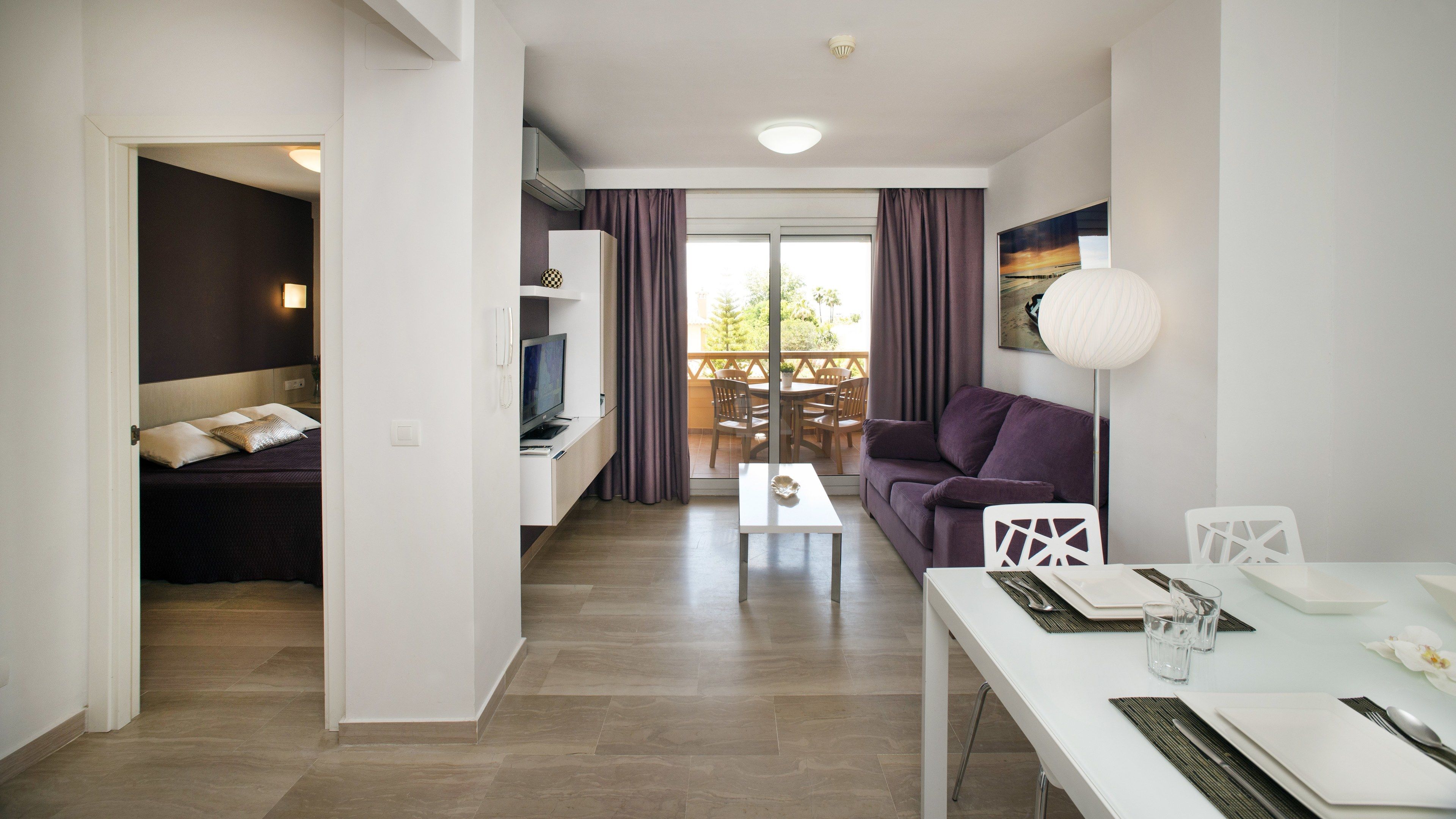 Una sala moderna con un sofá, una mesa de comedor para dos personas y un balcón con vistas.