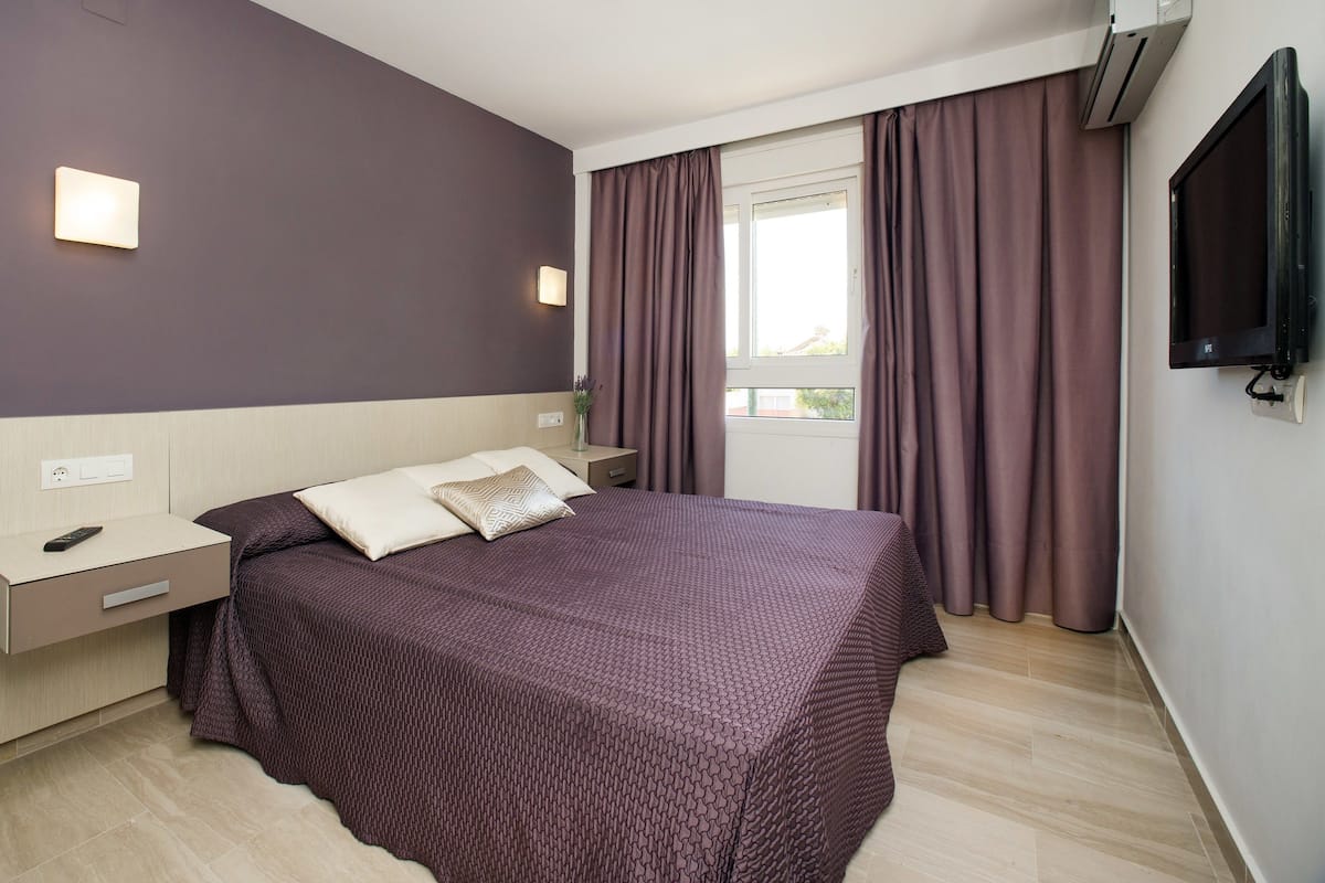Une chambre d’hôtel moderne dotée d’un grand lit, d’une table de chevet, d’un téléviseur à écran plat et d’une fenêtre avec des rideaux.