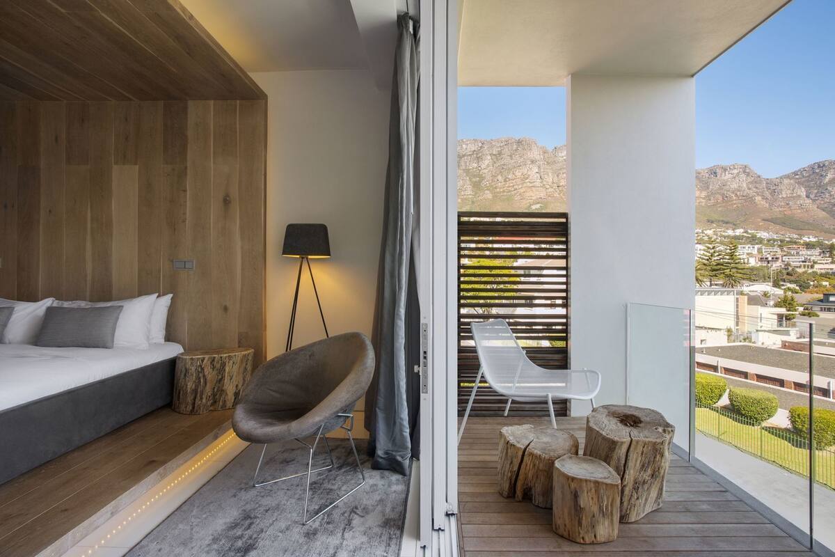 A balcony with a bed, a chair, a lamp, and a view of a cityscape.
