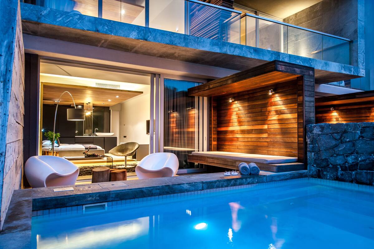 A modern outdoor pool area with a stone wall, wooden deck, and seating.
