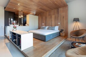 Un dormitorio moderno con una cama grande, una mesita de noche, una silla y un escritorio con espacio de almacenamiento.