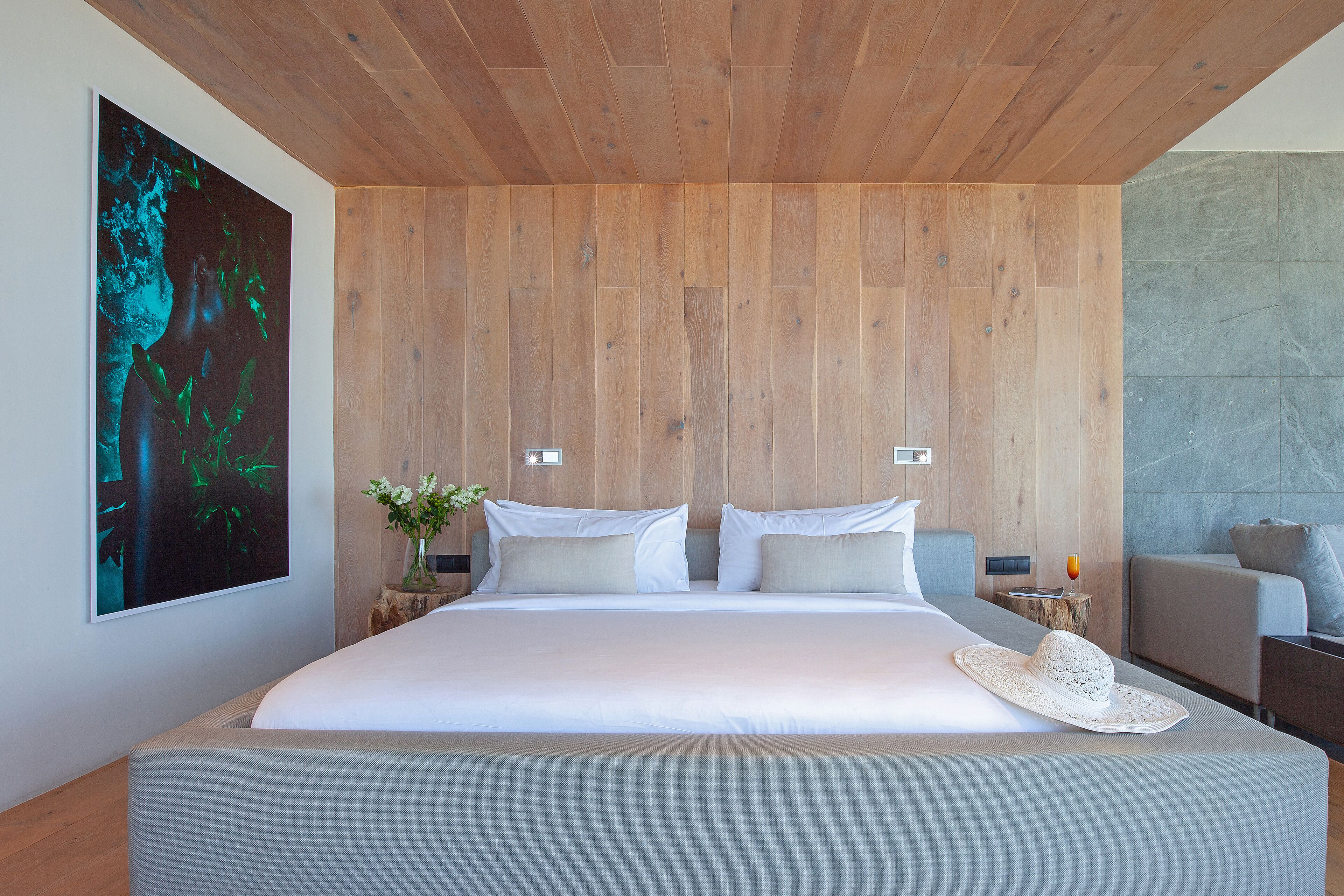 A modern bedroom with a large bed, wooden panel wall, and a painting.