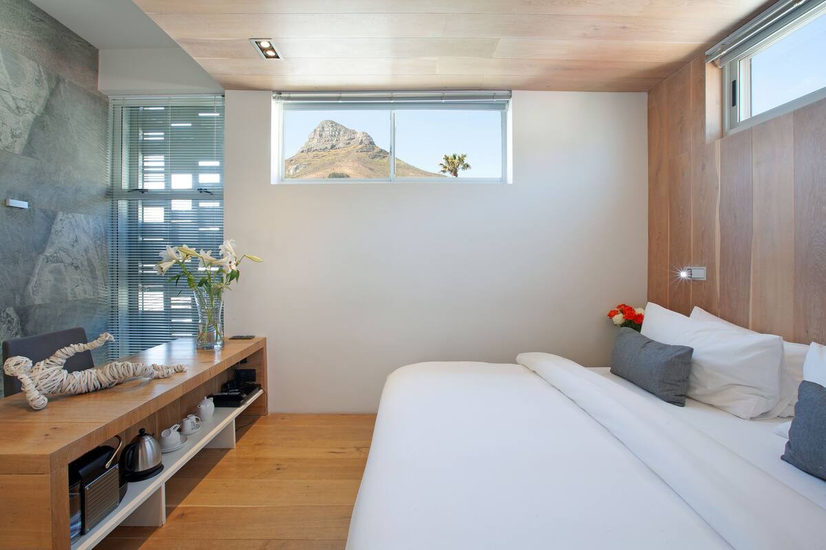 A bedroom with a bed, a wooden desk, and a window with a view of a mountain.