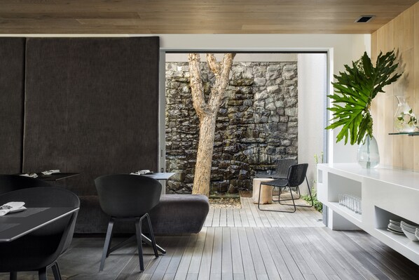 A modern outdoor dining area with a stone wall, wooden ceiling, and a large plant.
