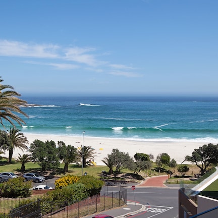 A coastal view from a balcony overlooking a beach with palm trees and a clear sky.