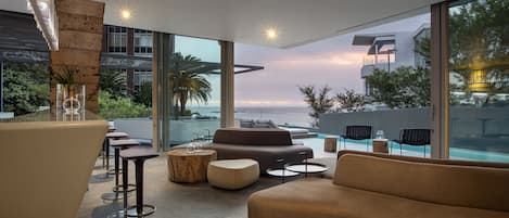 Un espacio lounge moderno al aire libre con un sofá, taburetes de bar y vista a la piscina.