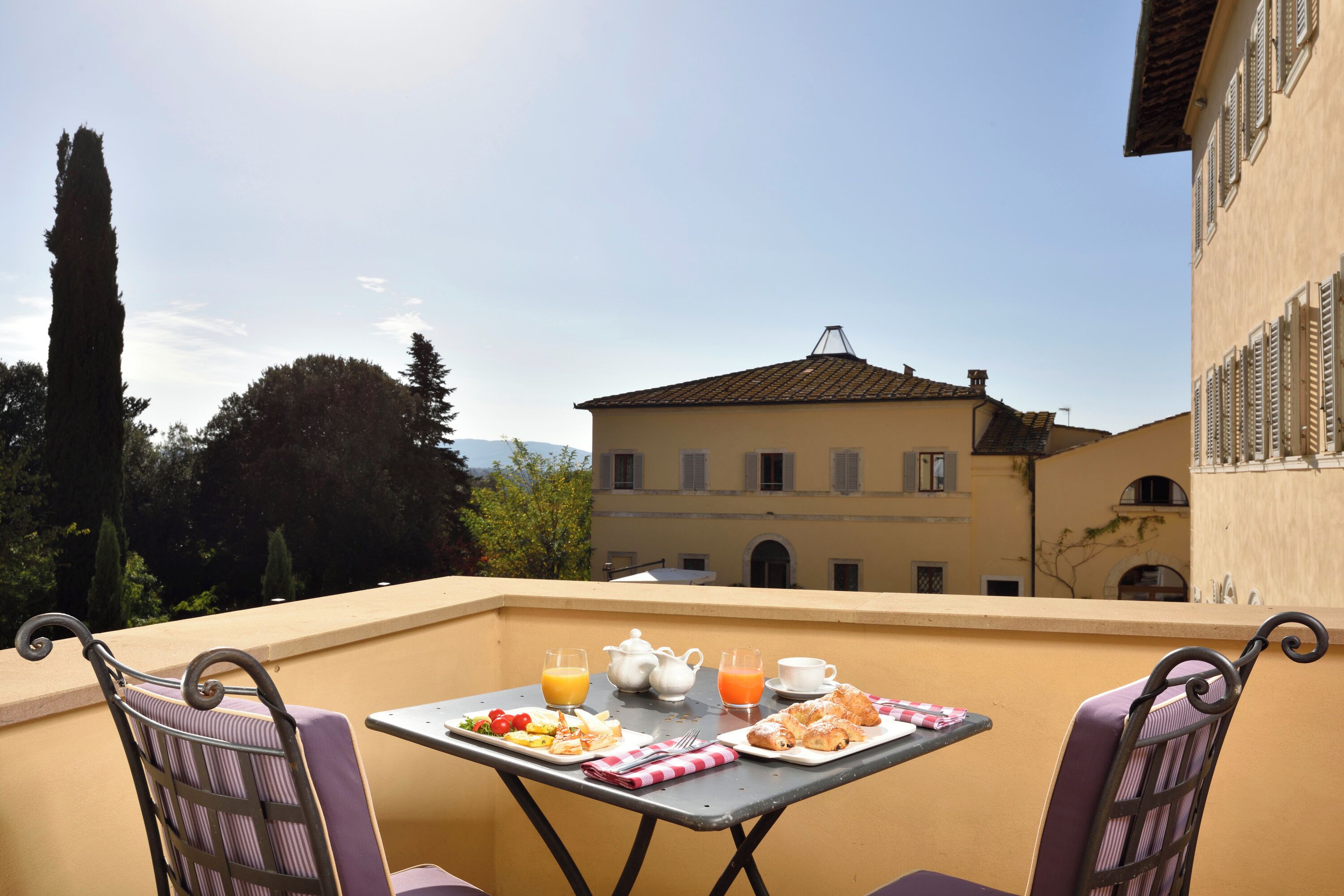 Un balcon avec une table préparée pour le petit-déjeuner, comprenant des assiettes de nourriture, une théière, des tasses et un verre de jus d’orange.