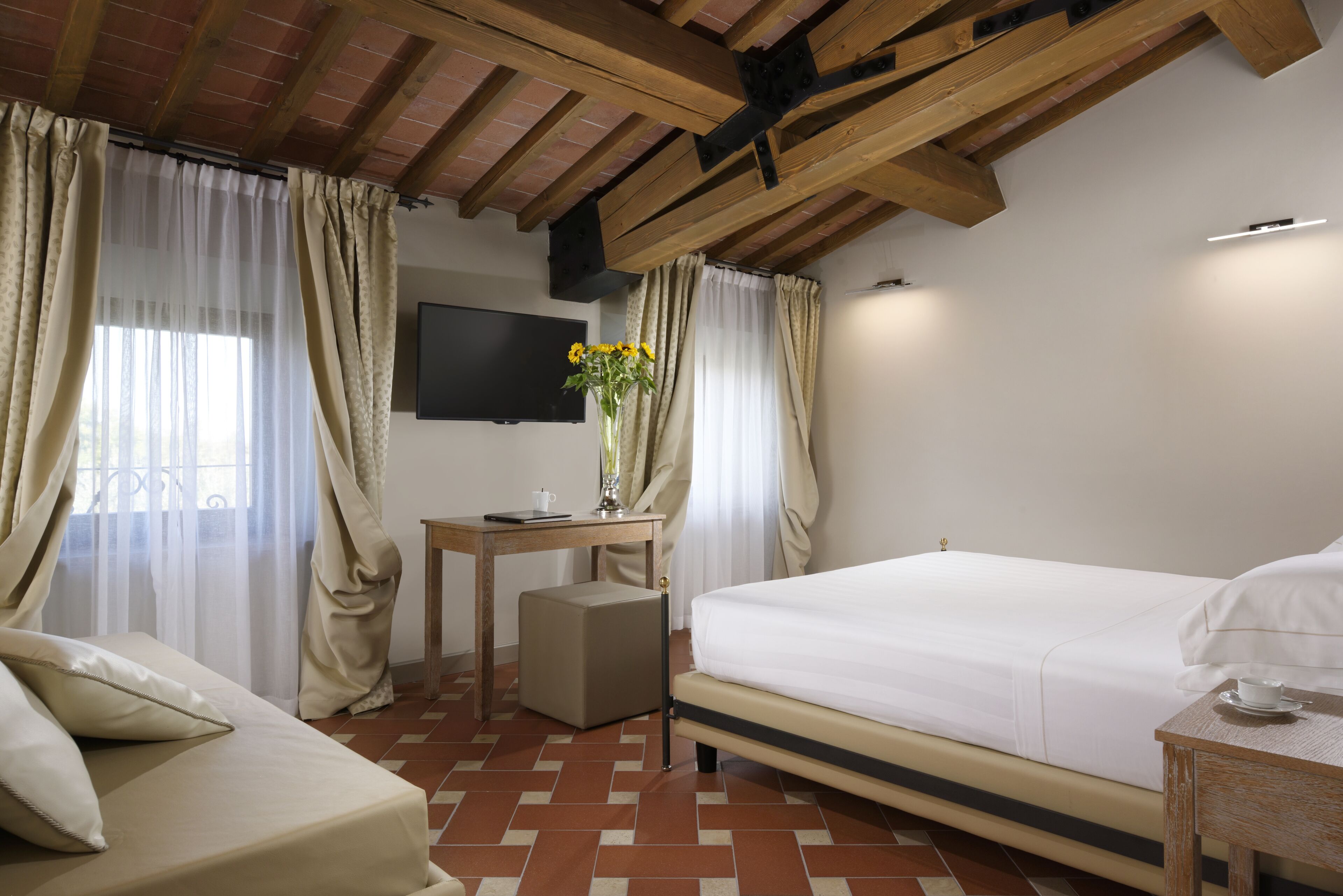 A hotel room with a bed, a desk, a chair, a TV, and curtains.