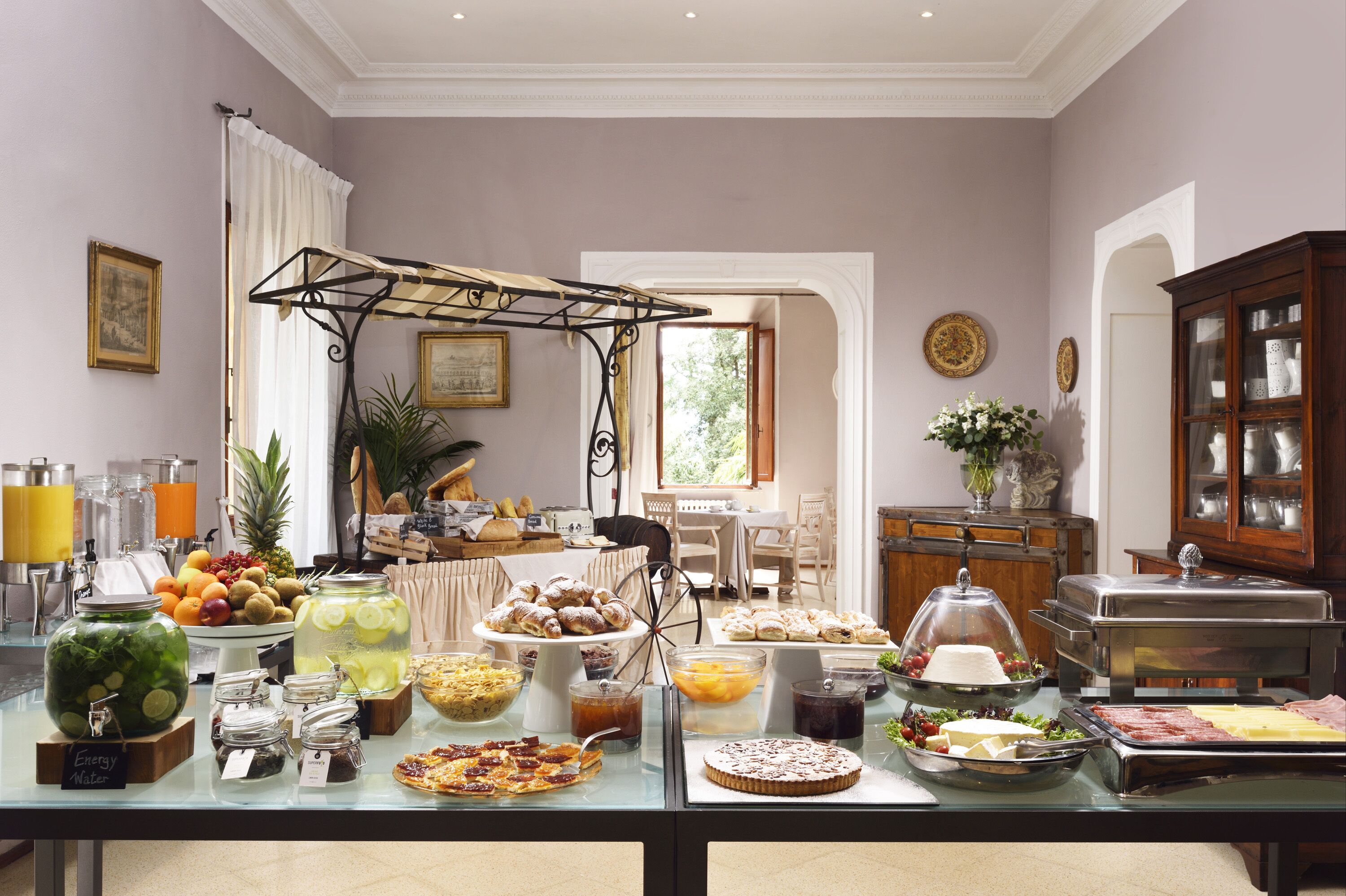 Ein reichhaltiges Buffet mit verschiedenen Speisen und Getränken, ein Essbereich mit Stühlen und Tisch sowie eine dekorative Vitrine.