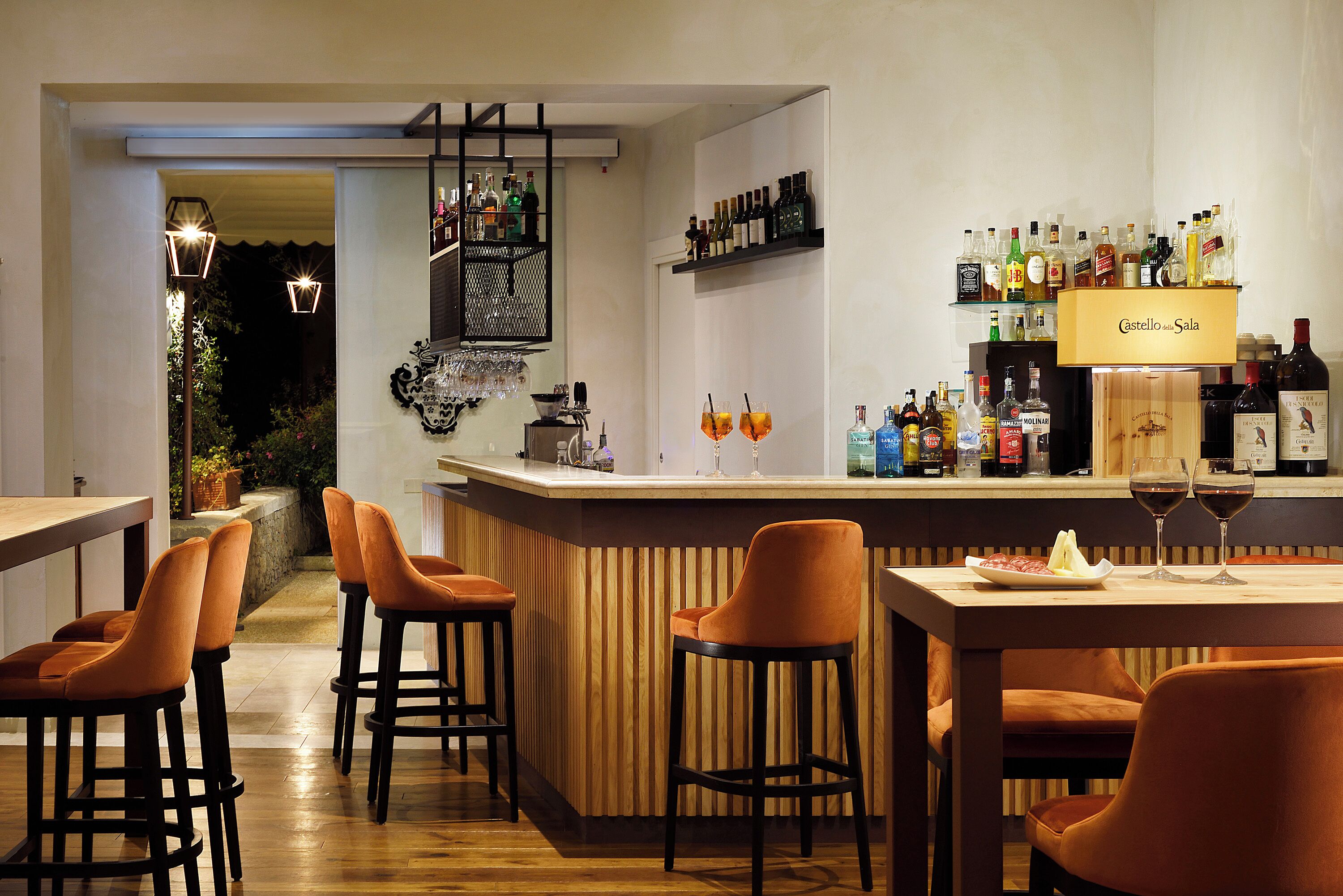 Eine Bar mit hölzernen Barhocker, einer Theke mit verschiedenen Flaschen und einem Schild mit der Aufschrift 'Castello & Sala'.