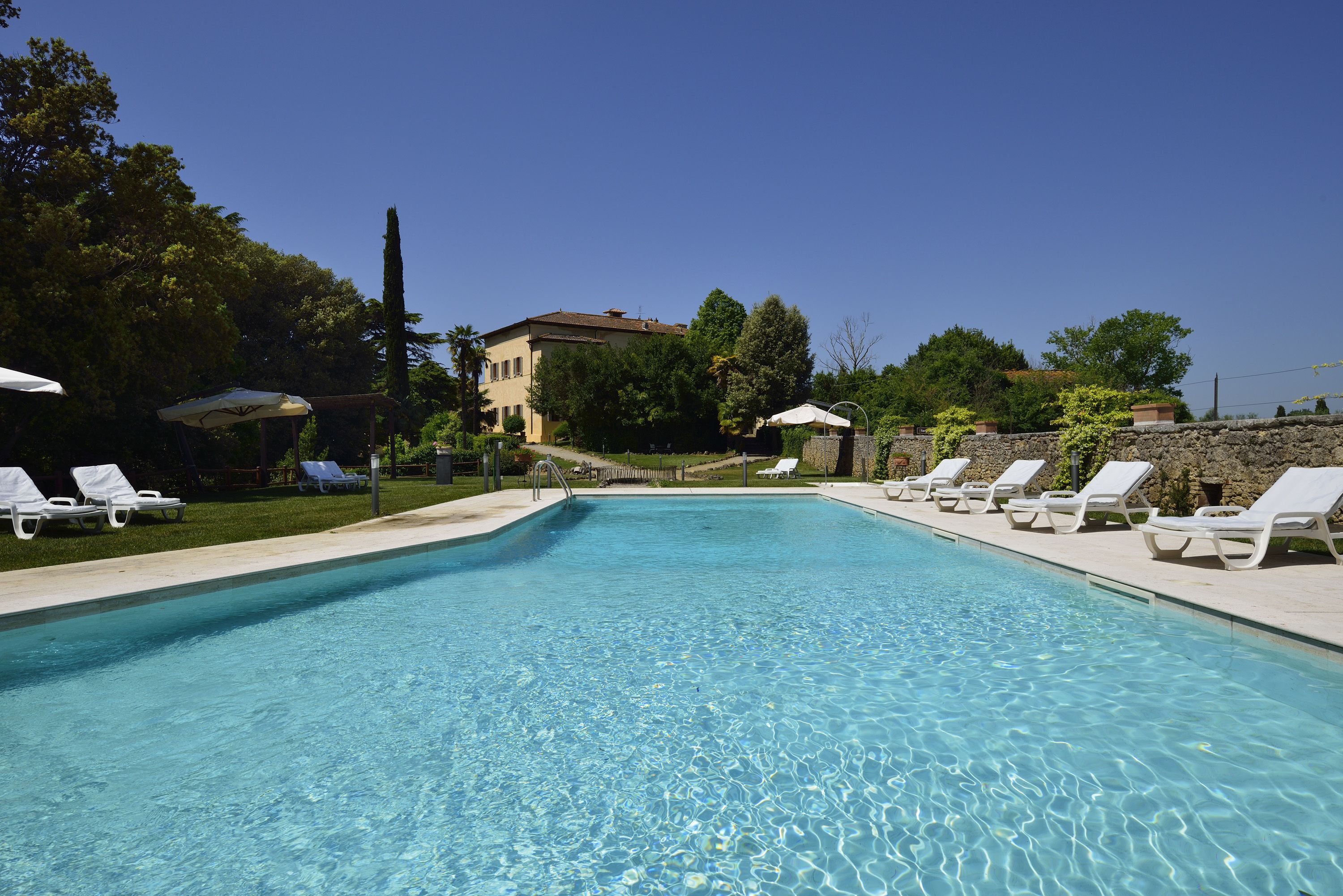 Una piscina con agua cristalina azul, rodeada de sillas de descanso blancas y sombrillas.