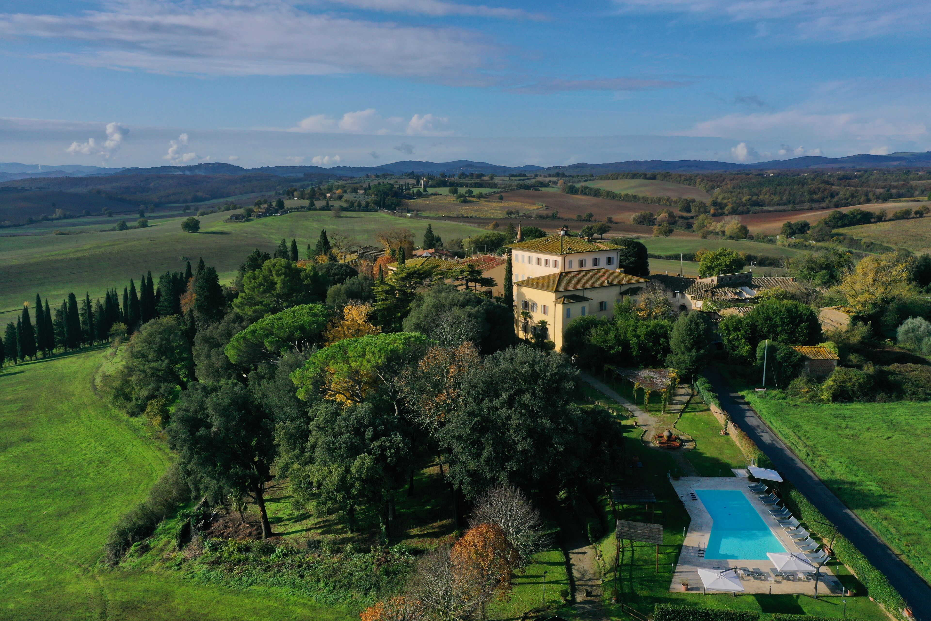 A large estate with a swimming pool, surrounded by lush greenery and hills in the background.