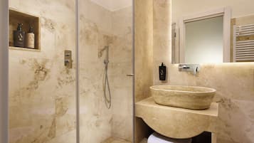 A bathroom with a glass-enclosed shower, a marble sink, and a shelf with toiletries.