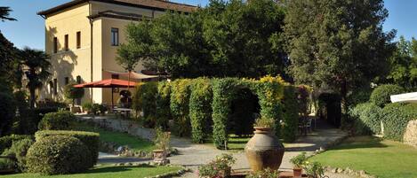 A building with a garden featuring a central circular area with a large vase, surrounded by greenery and a gravel path.