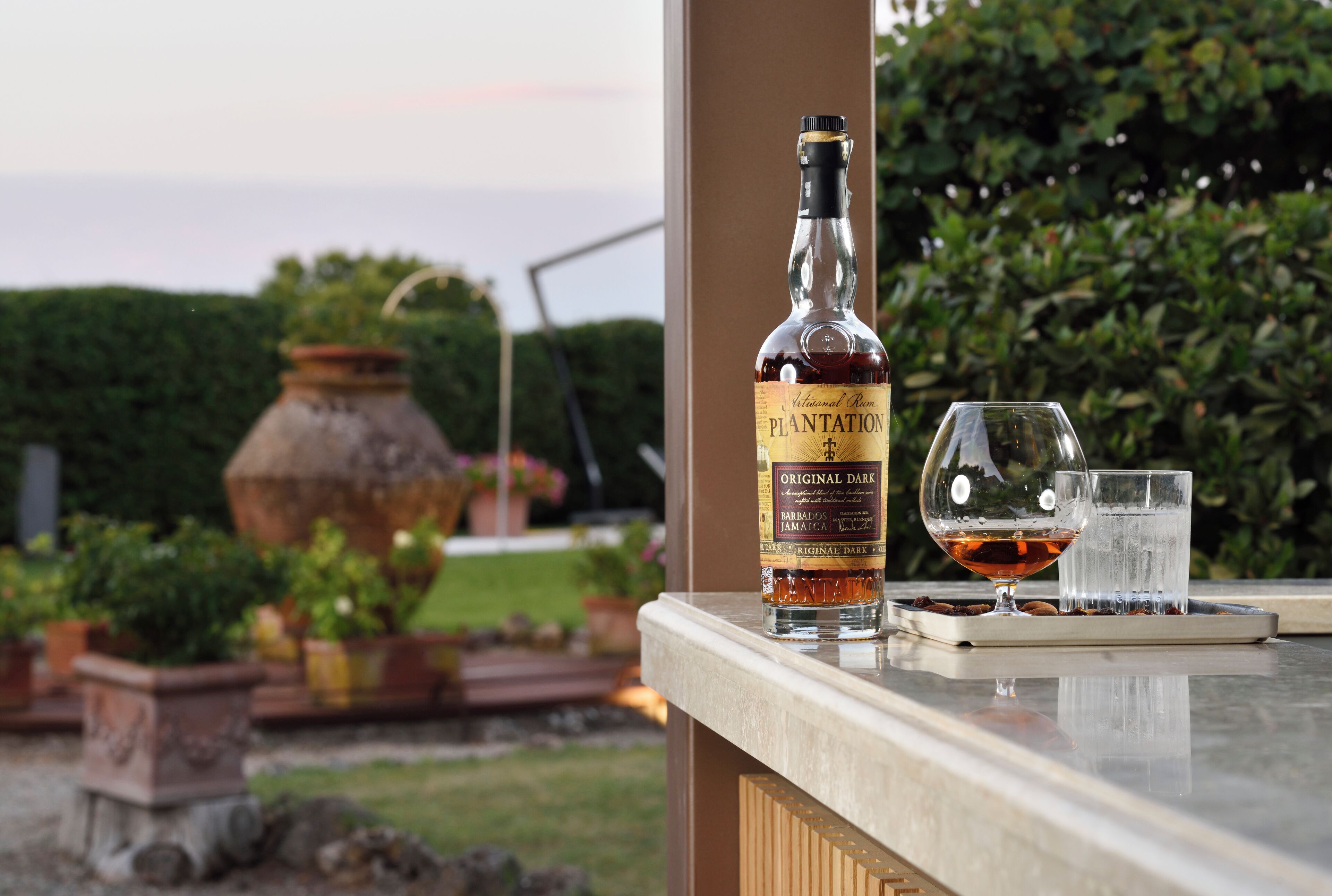Uma garrafa de rum Plantation Original Dark, um copo de rum e um copo de água sobre um tabuleiro.