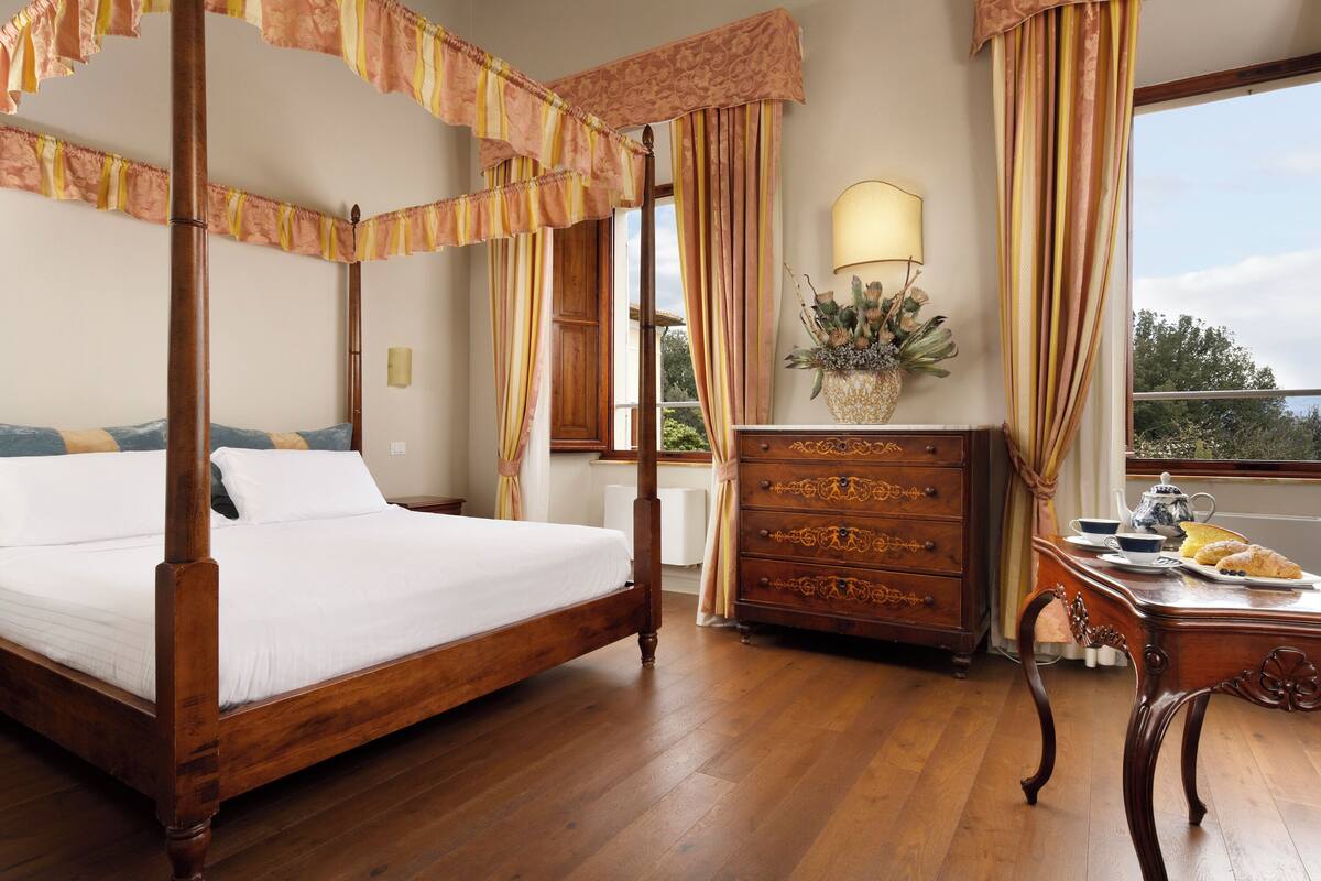 A four-poster bed with a wooden frame, a dresser with ornate carvings, and a window with curtains.