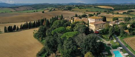 A villa with a swimming pool, surrounded by lush greenery and fields.