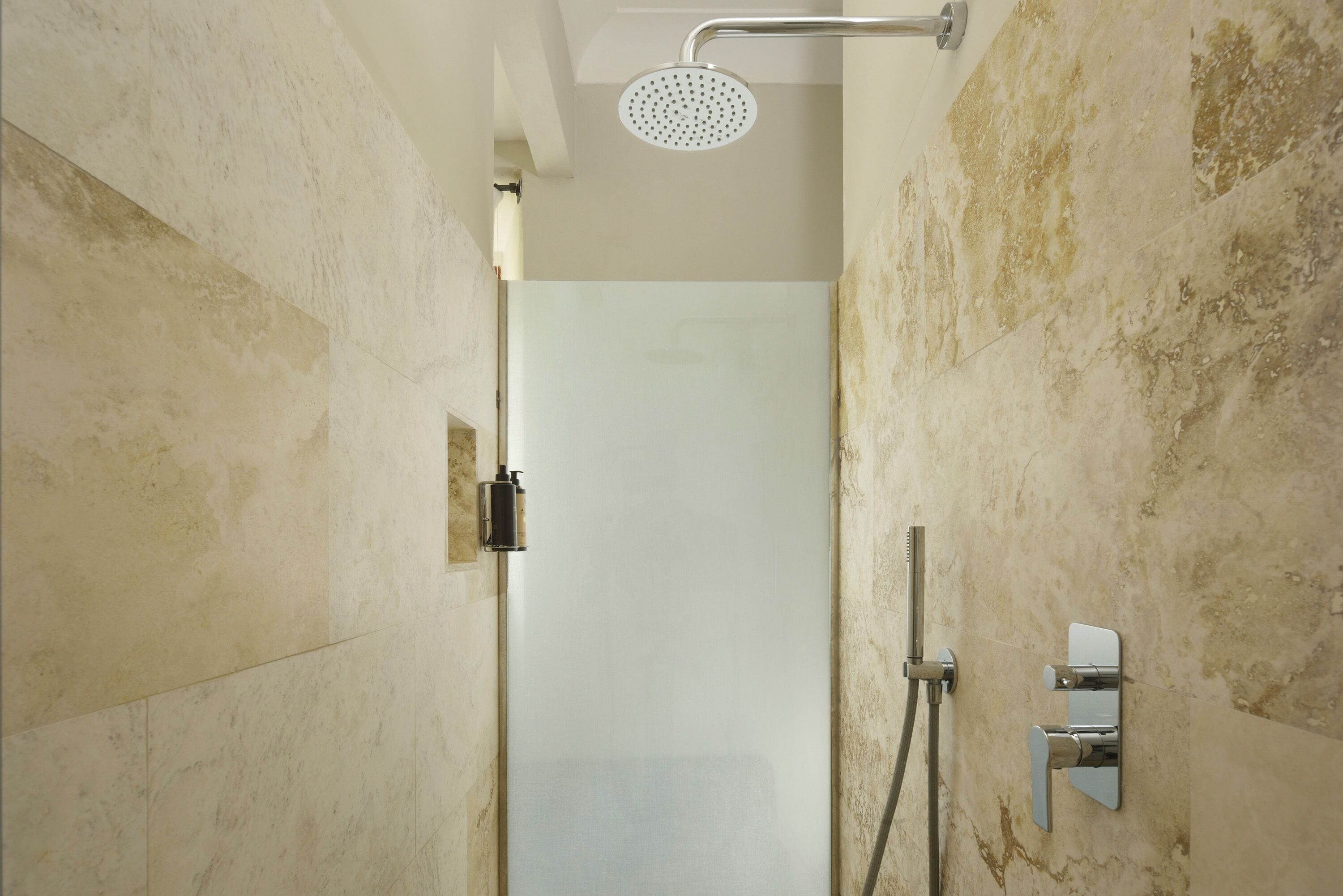 A shower with a handheld showerhead and a wall-mounted faucet.