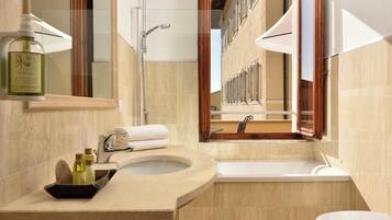 Un baño moderno con un lavamanos de mármol color crema, una bañera y un espejo grande.