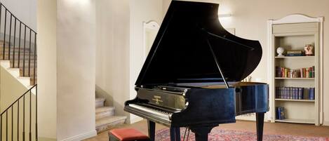 Un piano de cola en una habitación amplia con una escalera y una estantería.
