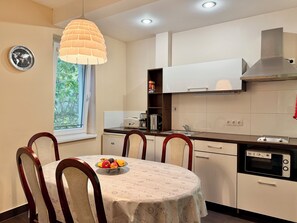 A modern kitchen with white cabinets, a built-in oven, and a dining area with a round table and chairs. - Gold Apartments (Budapest)