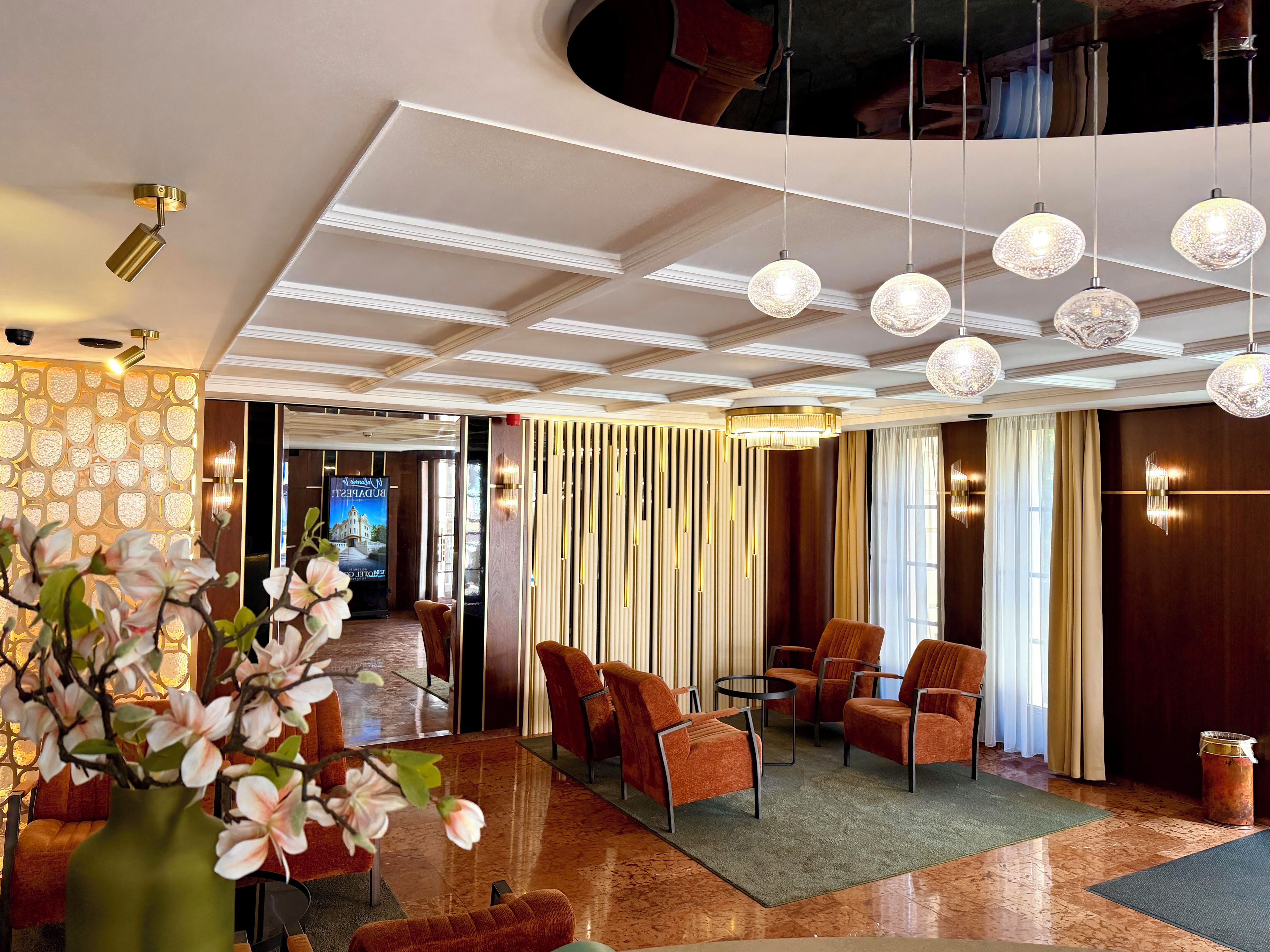 Un hall d’hôtel au design moderne, comprenant un espace salon avec des fauteuils et un vase de fleurs.
