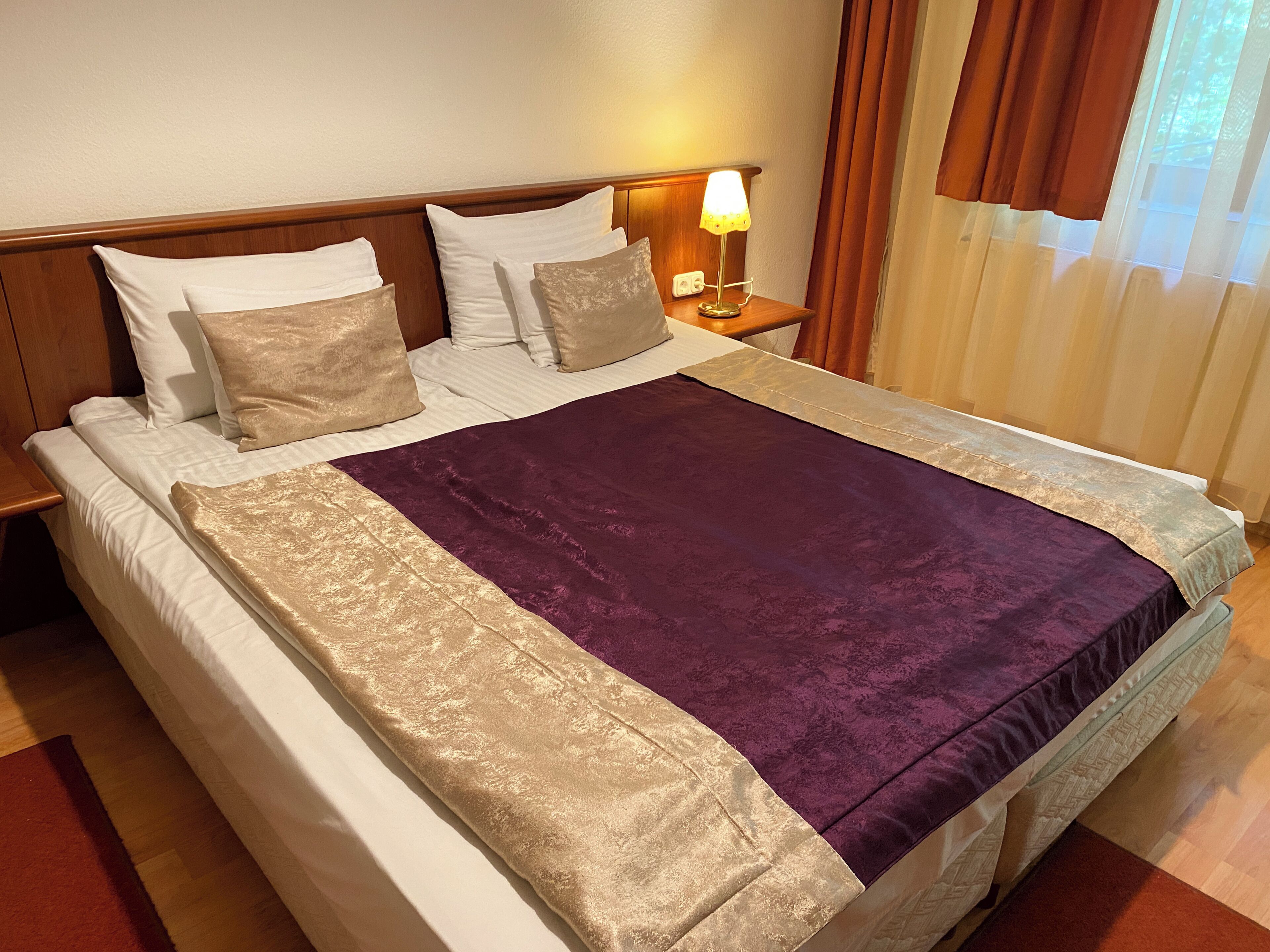 A neatly made bed with a purple and gold bedspread, white linens, and a wooden headboard.