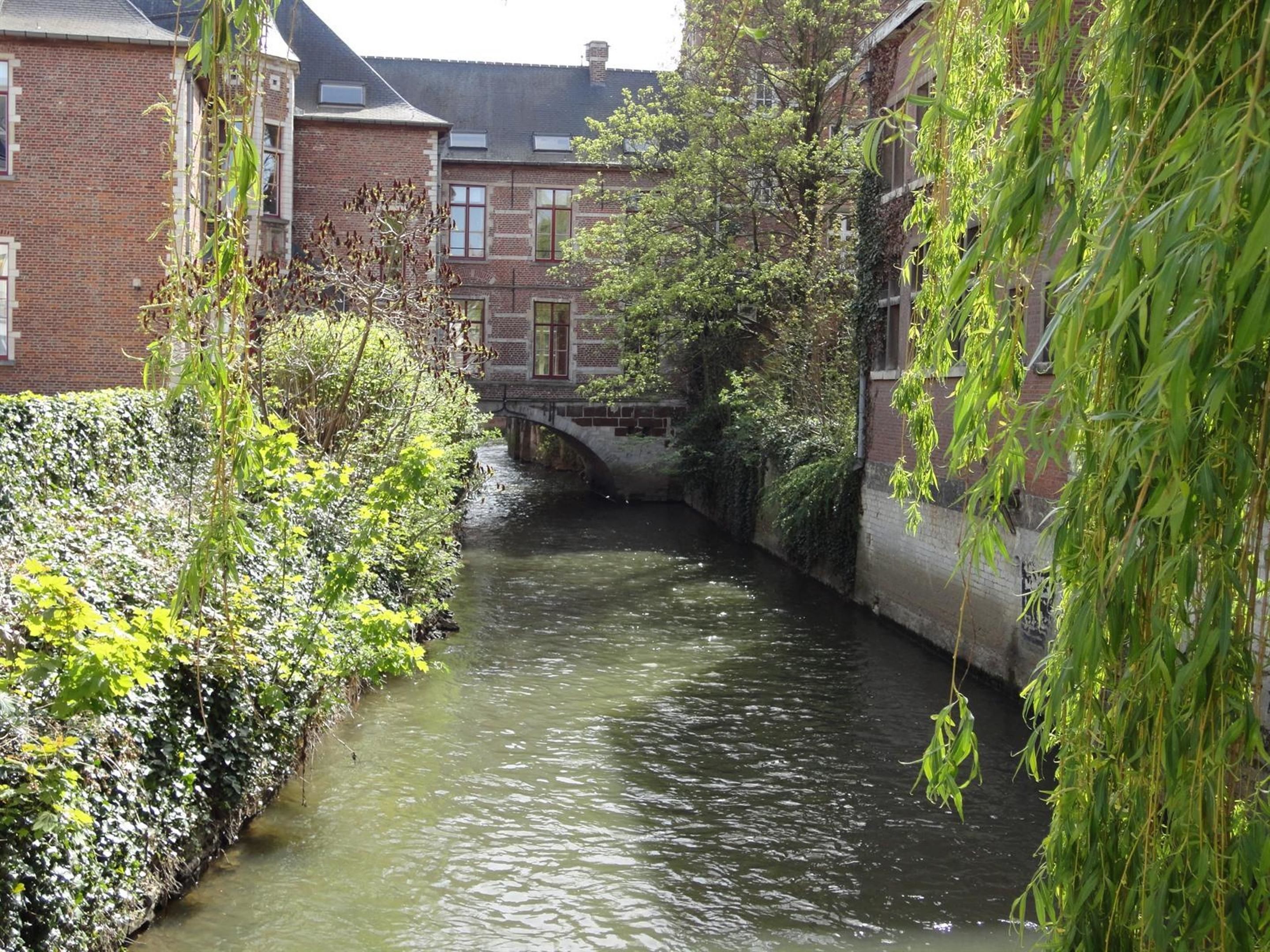 A narrow canal flanked by buildings and greenery, with a bridge crossing the water.