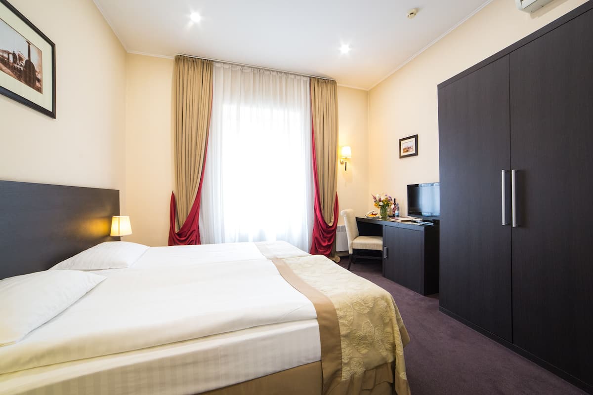 A hotel room with a bed, a desk, a wardrobe, and a window with curtains.