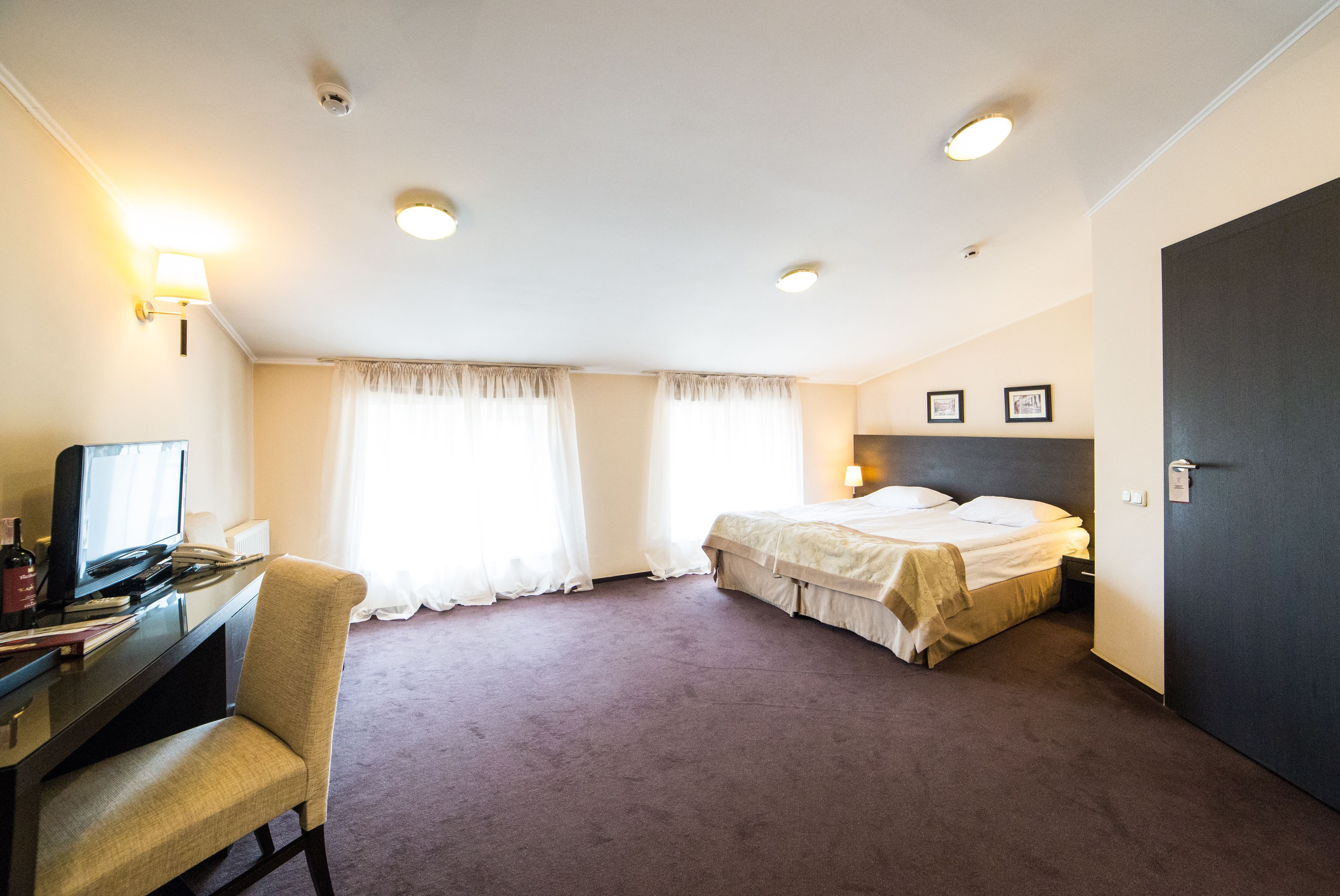 A hotel room with a bed, a desk with a chair, a television, and two bedside lamps.