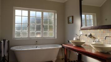 A bathroom with a freestanding bathtub, a double sink vanity, a large mirror, and a window with frosted glass panes.