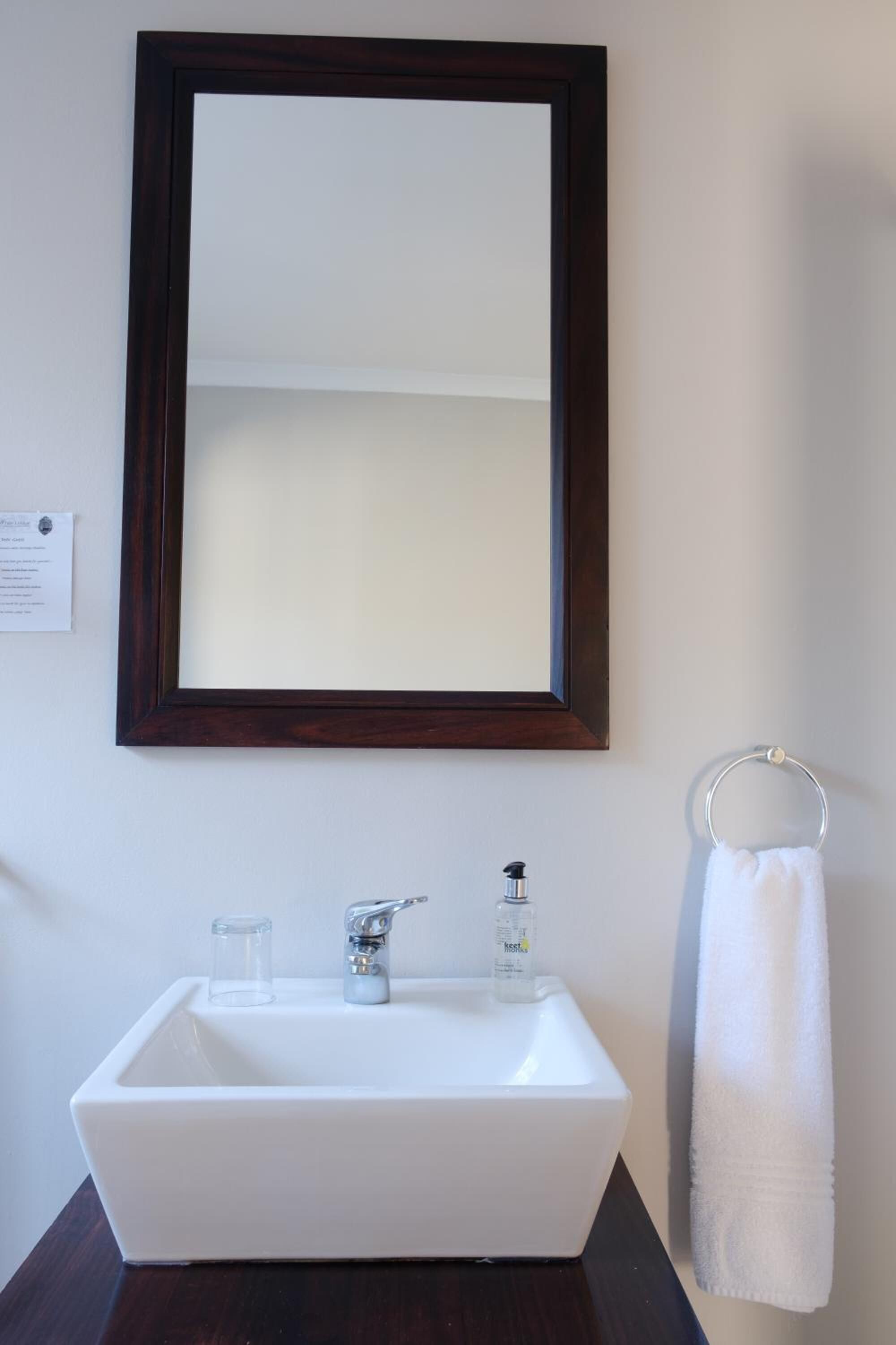 A bathroom with a white sink, a dark wooden frame mirror, a white towel, and a small glass container.