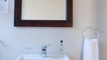 Un bagno con un lavandino bianco, uno specchio con cornice in legno scuro, un asciugamano bianco e un piccolo contenitore in vetro.