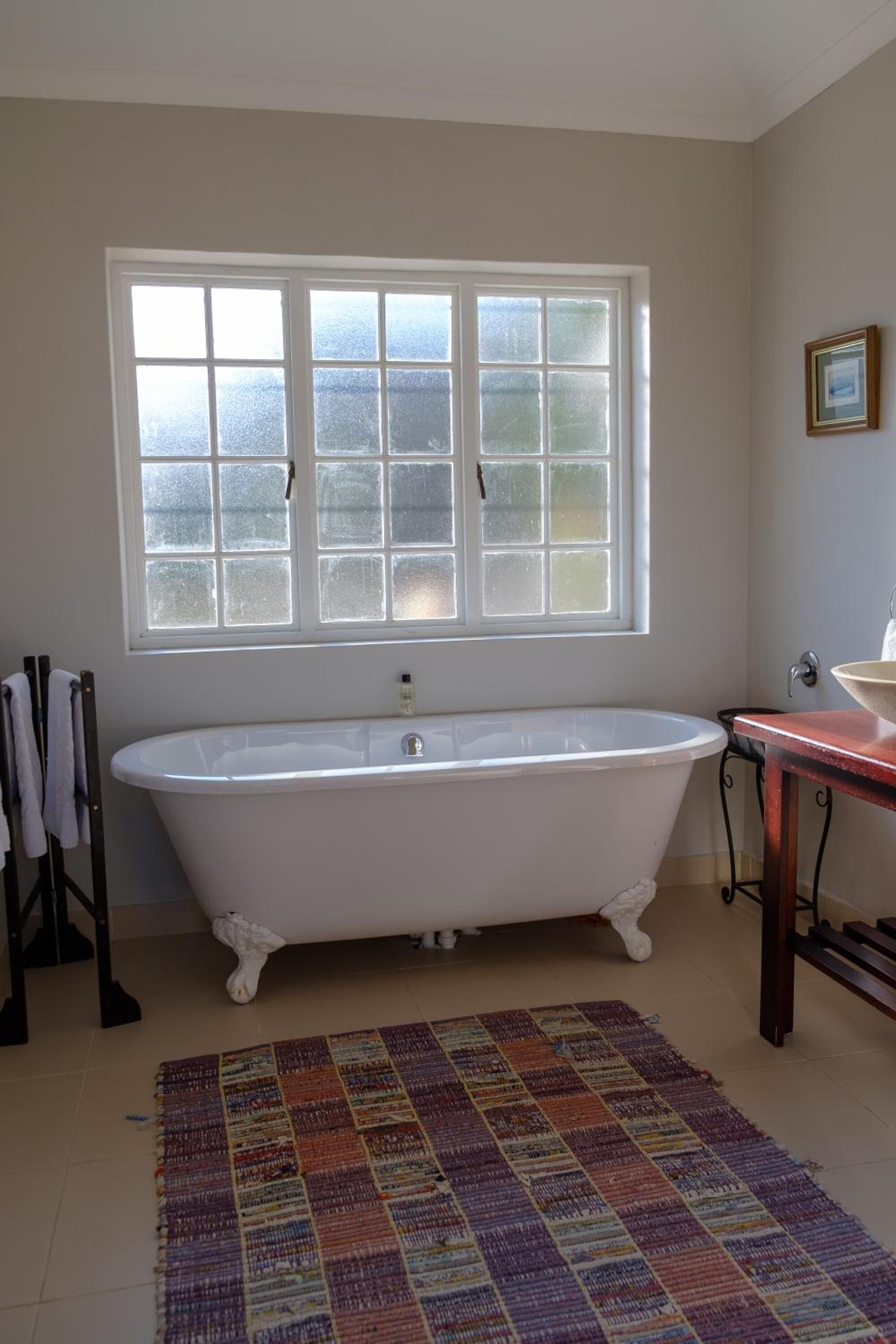 A bathroom with a freestanding bathtub, a window with frosted glass, a sink, and a patterned rug.