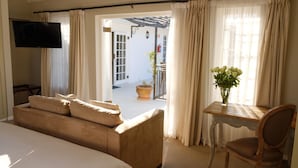 Ein Hotelzimmer mit Bett, Wand-Fernseher, Holztisch mit Stuhl und Blick auf den Außenbereich durch eine Tür.