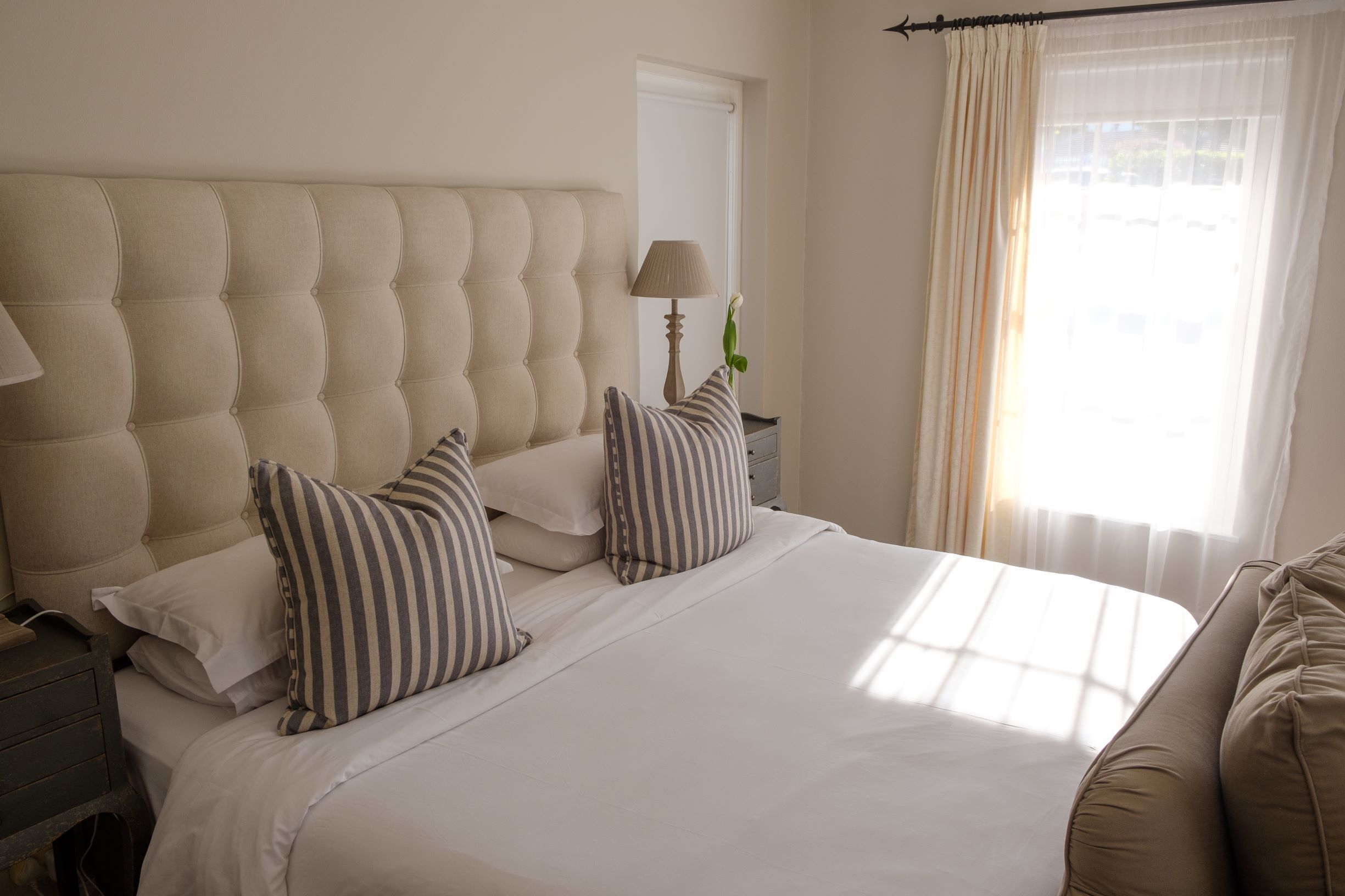 A neatly made bed with striped pillows, a tufted headboard, and a bedside lamp.