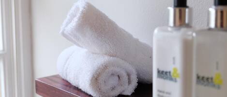 A white towel rolled up on a wooden shelf next to two bottles of lotion.