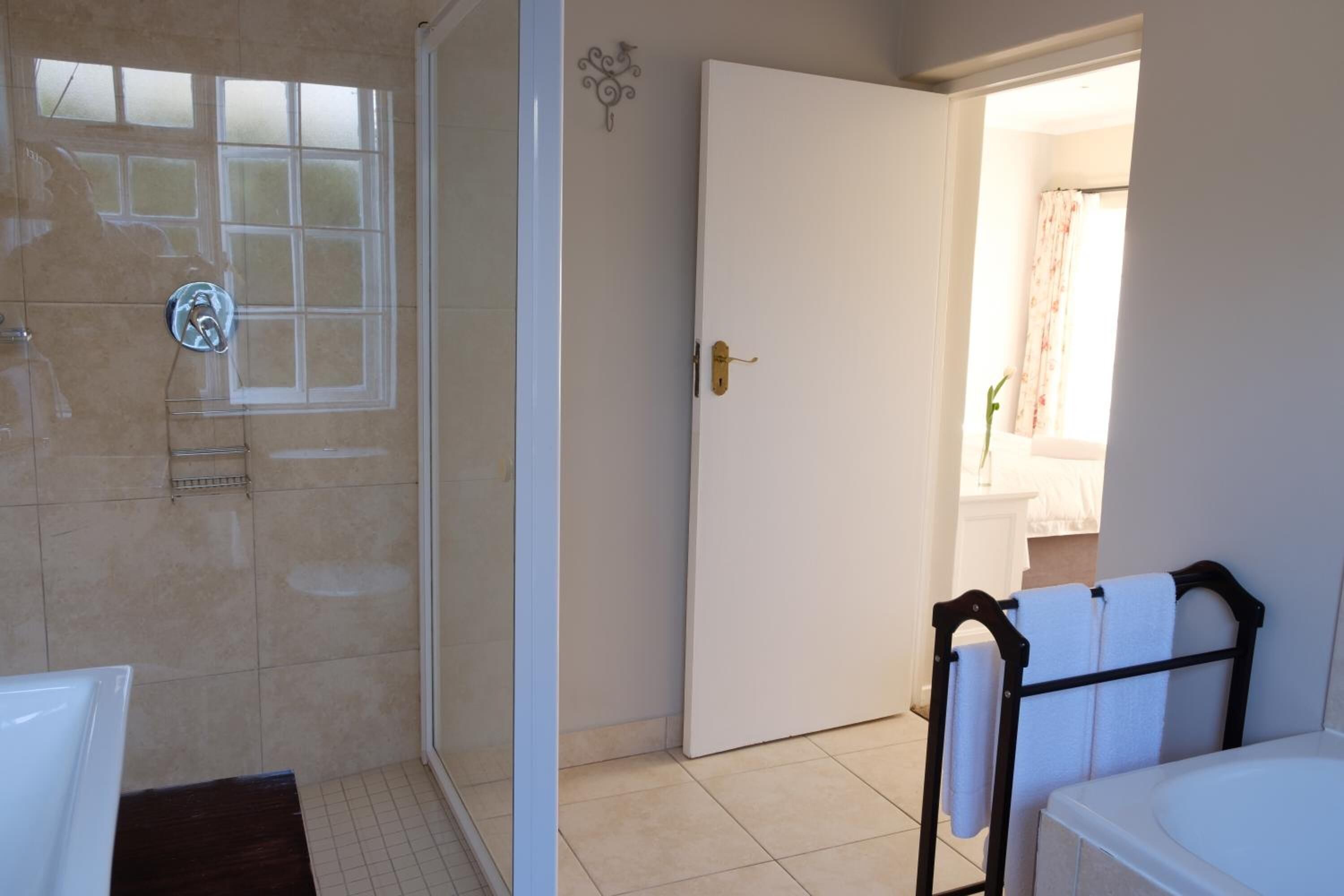 A bathroom with a bathtub, a shower, and a door leading to a bathroom with a toilet and sink.