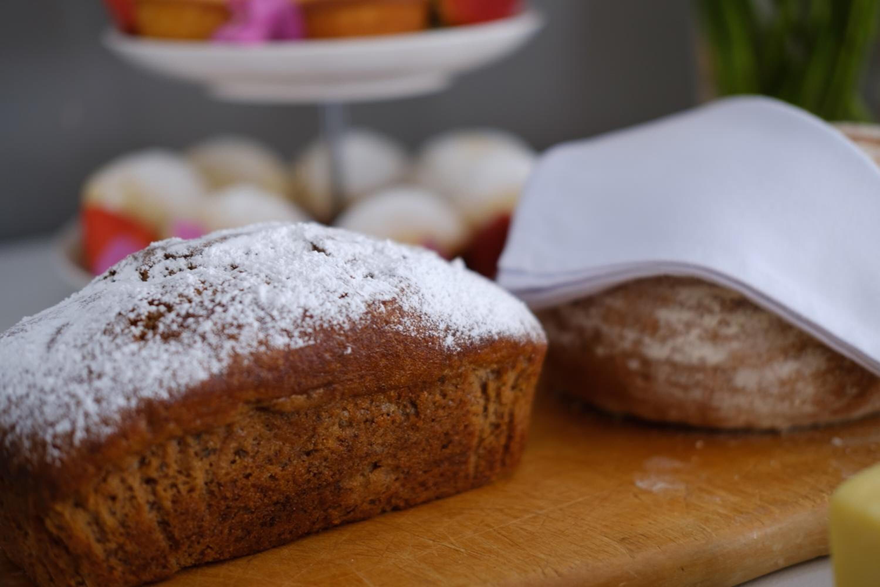 Een broodje bestrooid met poedersuiker op een houten snijplank.
