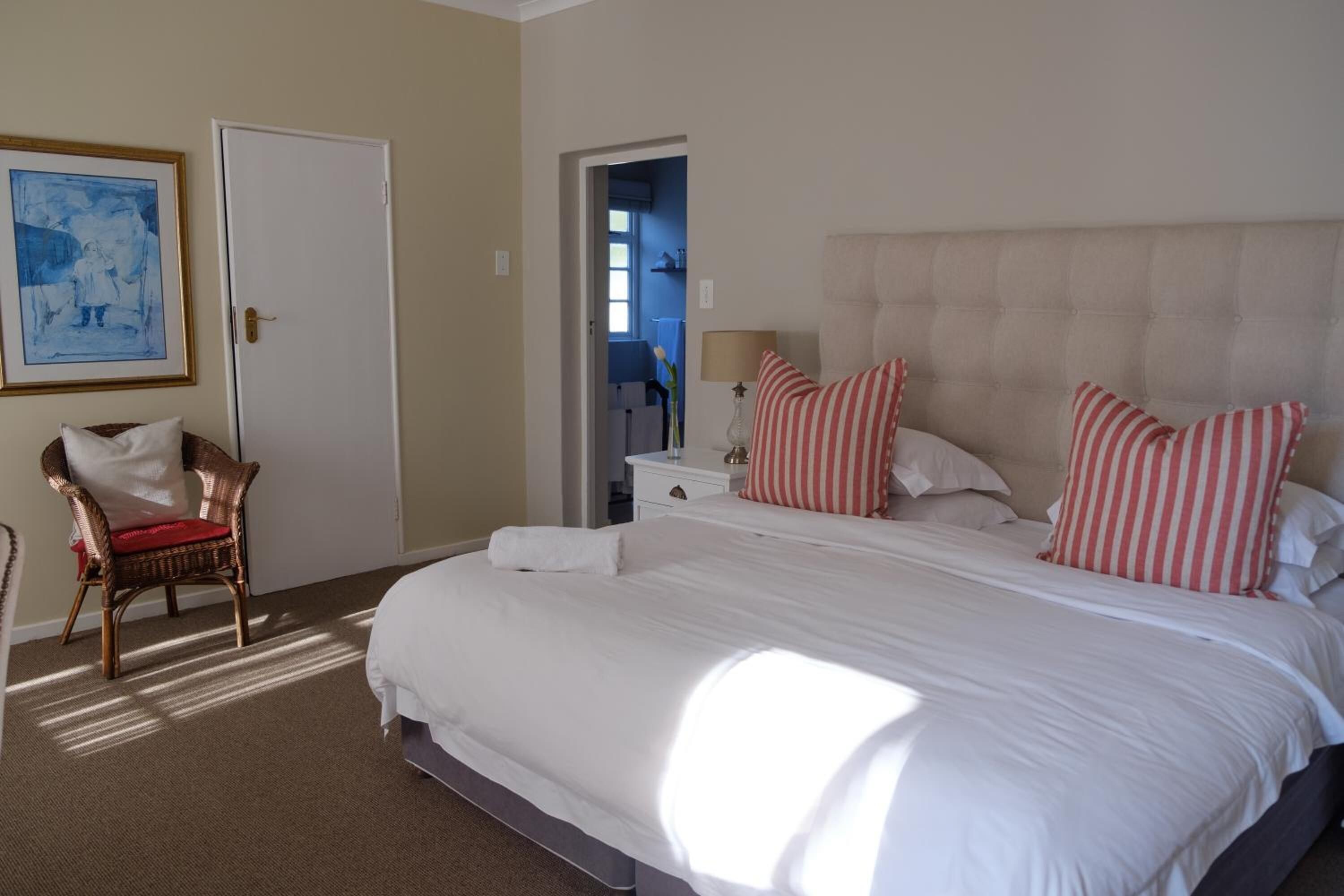 A hotel room with a large bed, a chair, a door, and a painting on the wall.