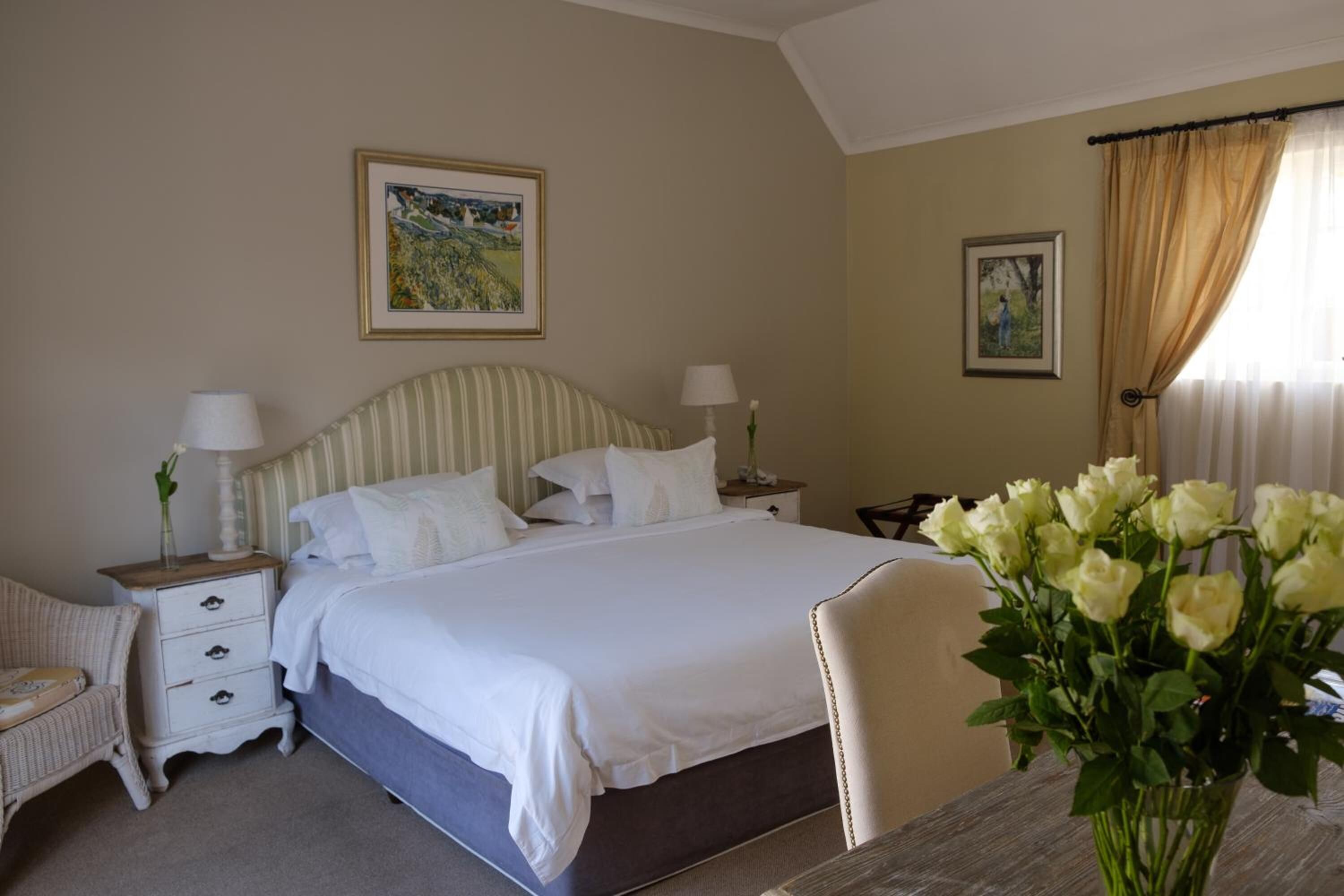 A neatly arranged bedroom with a bed, bedside tables, a chair, and a vase of flowers.