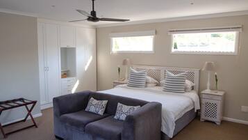 Une chambre à coucher comprenant un lit, deux tables de chevet, un ventilateur de plafond et une fenêtre avec des stores.