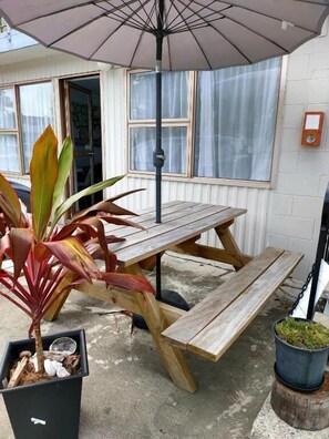 Un espacio de patio al aire libre con una mesa y bancos de madera, una planta en maceta y un paraguas colgante.