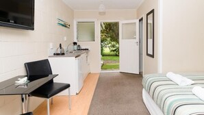 A compact hotel room with a bed, a small kitchenette, a dining area, and a view of the outdoors. - Aarangi Tui Motel (Paihia)