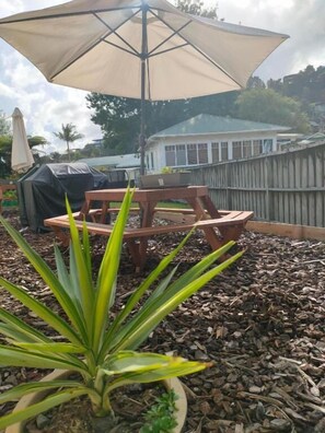 Un espacio de patio al aire libre con una mesa y sillas de madera, un paraguas grande y una planta en maceta.