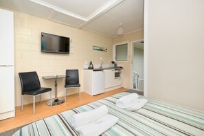 Una habitación compacta con cama, una kitchenette pequeña, un televisor montado en la pared y una ventana.